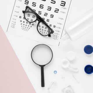 Eye chart, eyeglasses, magnifying glass, contact lens case, and solution bottle on a white and pastel pink background.