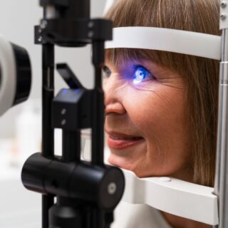 A woman undergoing an eye examination with a slit lamp, as a bright blue light illuminates her eye during the check-up.