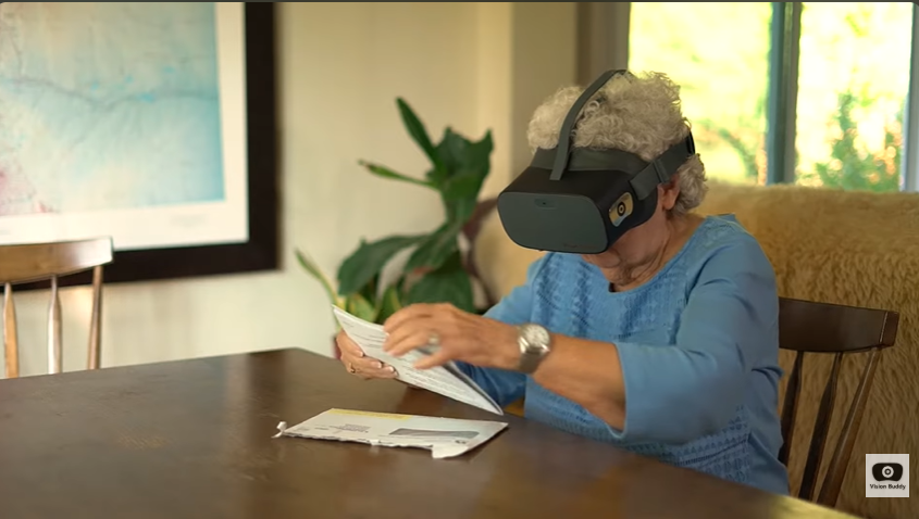 Doreen wearing her Vision Buddy headset, reading her mail at the kitchen table