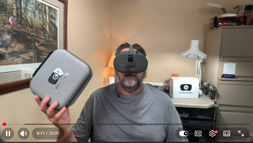 A legally blind veteran wearing the Vision Buddy VB4 Max, holding its carrying case