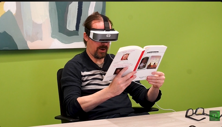 A reviewer wearing the Vision Buddy Mini headset, reading a book